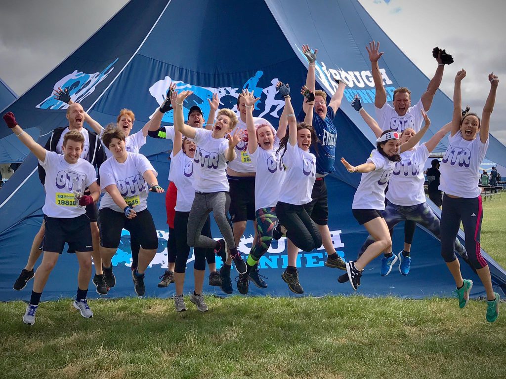 A group of people jump in the air with arms raised, wearing OTR t-shirts. 